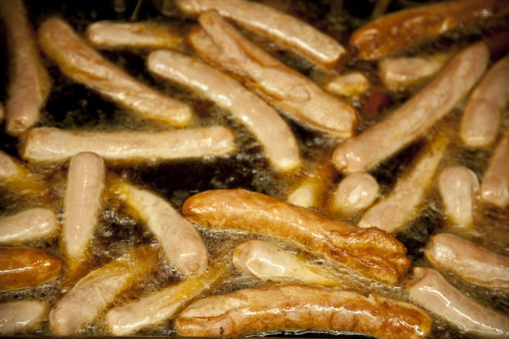 Several hot dogs frying in oil.