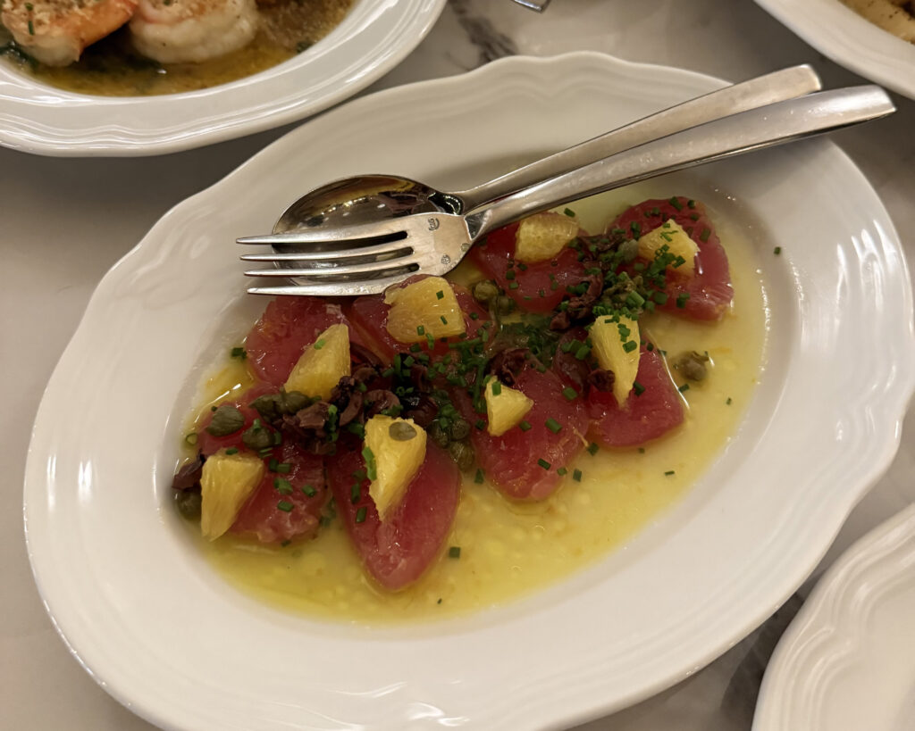 vibrant tuna crudo with segments of orange, EVOO, olives and capers