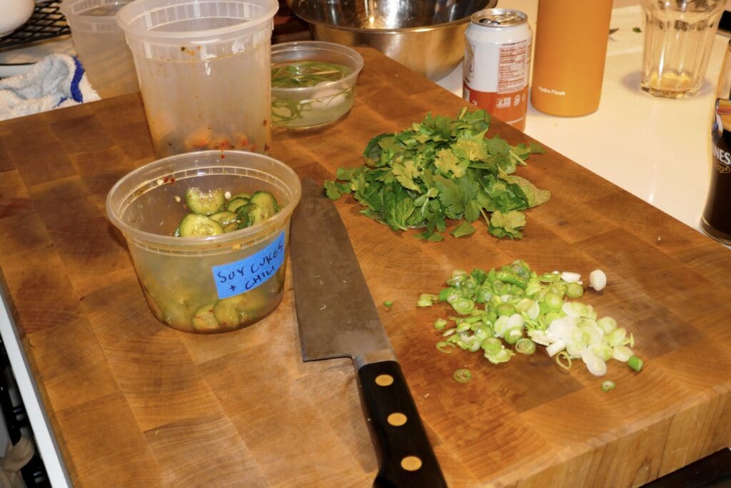 Prep, prep and more prep. sliced scallions, marinated cucumber, cut herbs and a knife all placed on cutting board