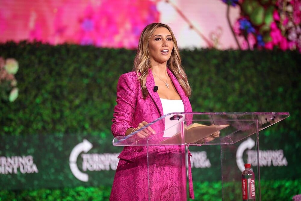 Alina Habba in a pink suit speaking at a Turning Point USA event