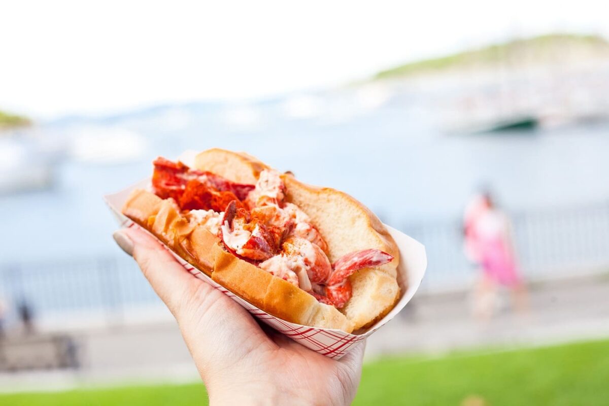 A lobster roll held up against a waterfront backdrop on a summer day in New Jersey