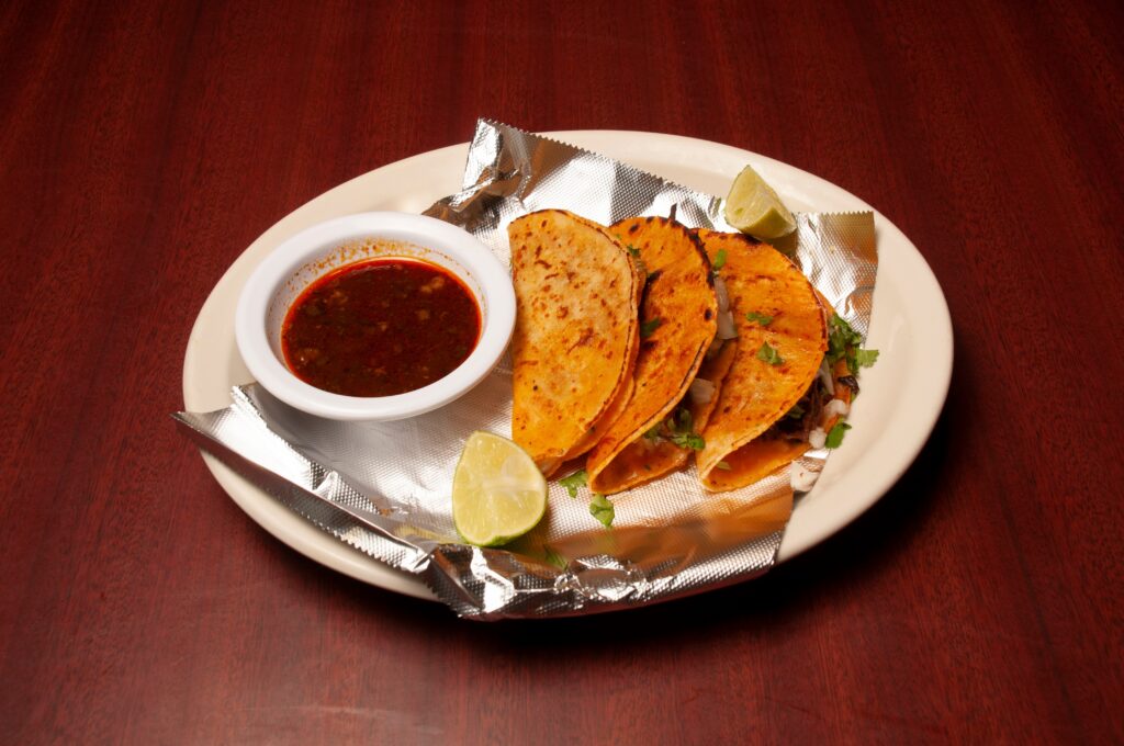 Birria tacos served with a cup of consommé and lime on a plate