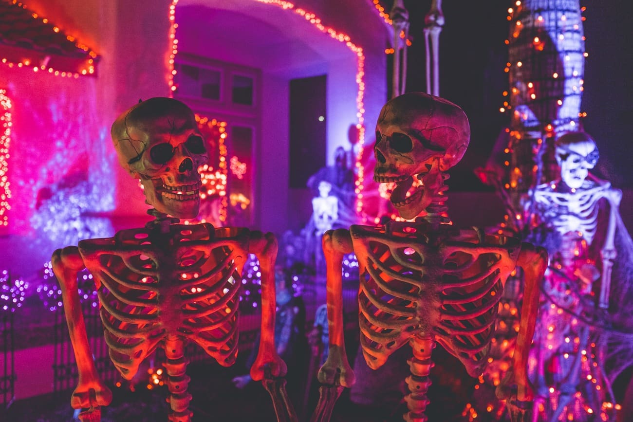 Halloween decorations featuring two skeletons standing near a white concrete building adorned with string lights