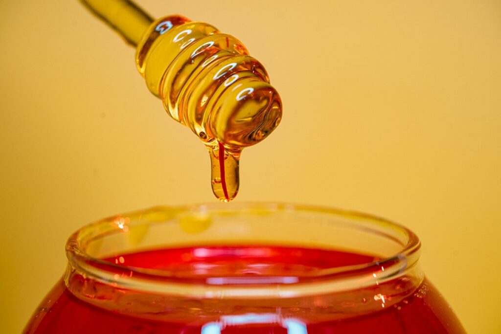 Raw honey dripping from a honey dipper into a glass jar