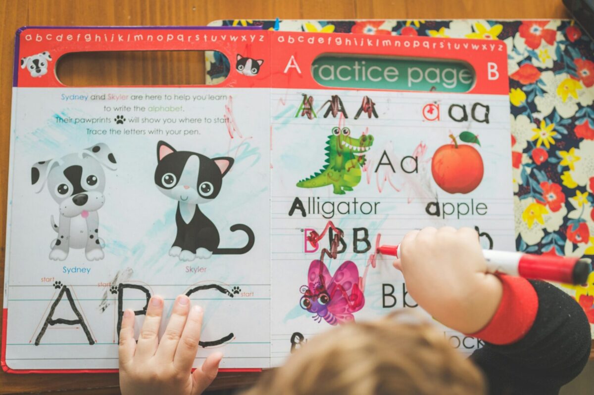 A young child tracing letters in an alphabet workbook at a preschool or early learning setting
