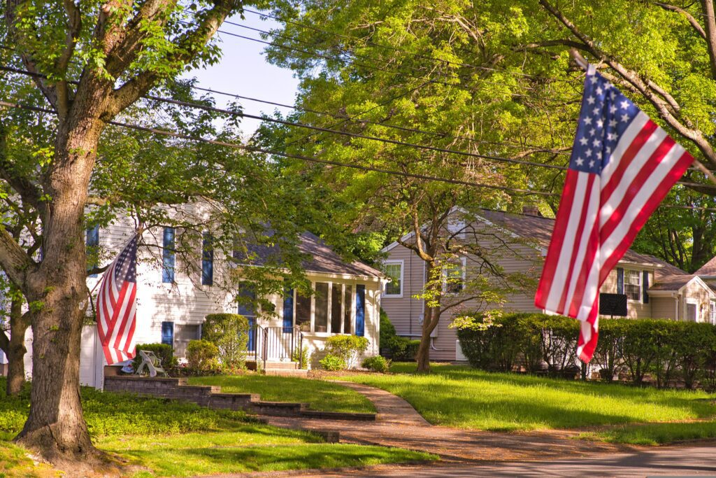 A tree-lined suburban street in New Jersey with American flags and residential homes
