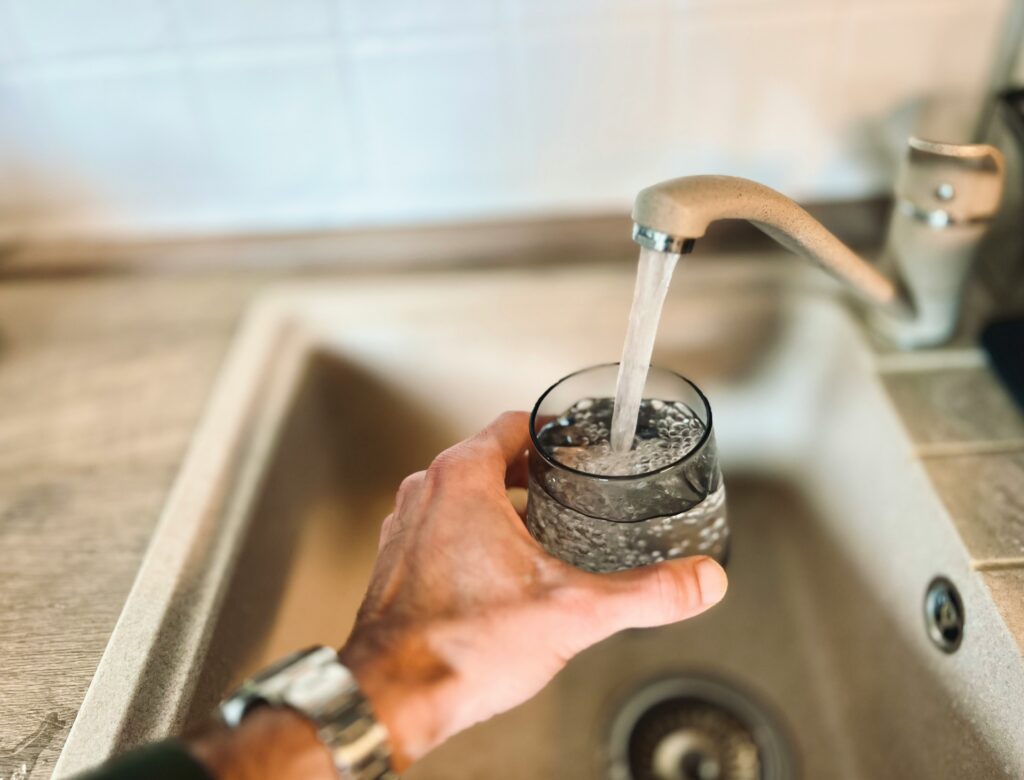 A glass of tap water being filled at a kitchen sink