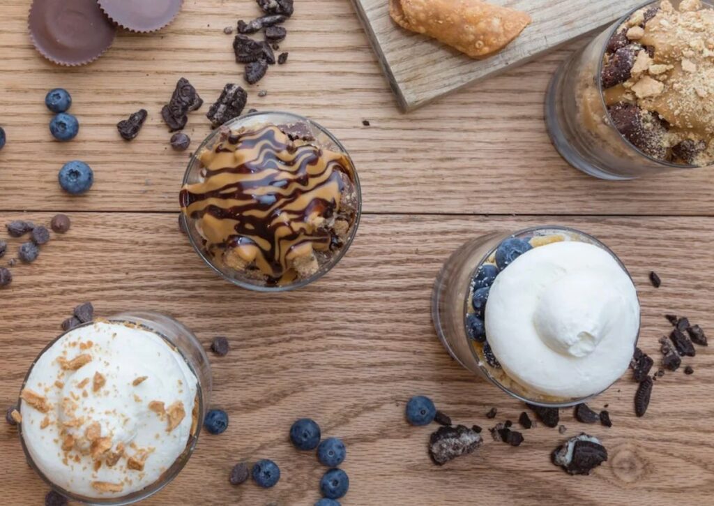 Four loaded ice cream sundaes from Scoop N Scootery in Red Bank, New Jersey, displayed on a wooden surface with toppings