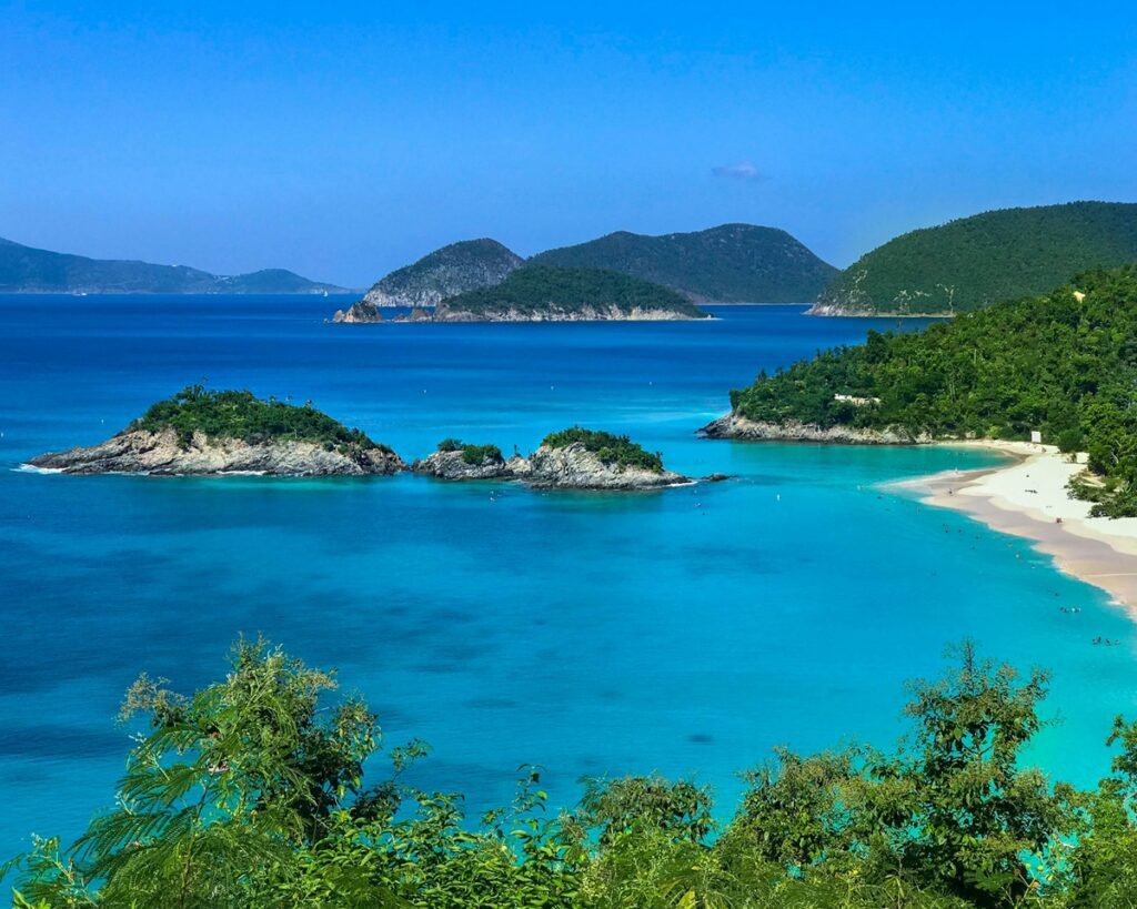 Aerial view of Trunk Bay in St. John, U.S. Virgin Islands, showing turquoise Caribbean water, white sand beach, and small rocky islands surrounded by lush green hills