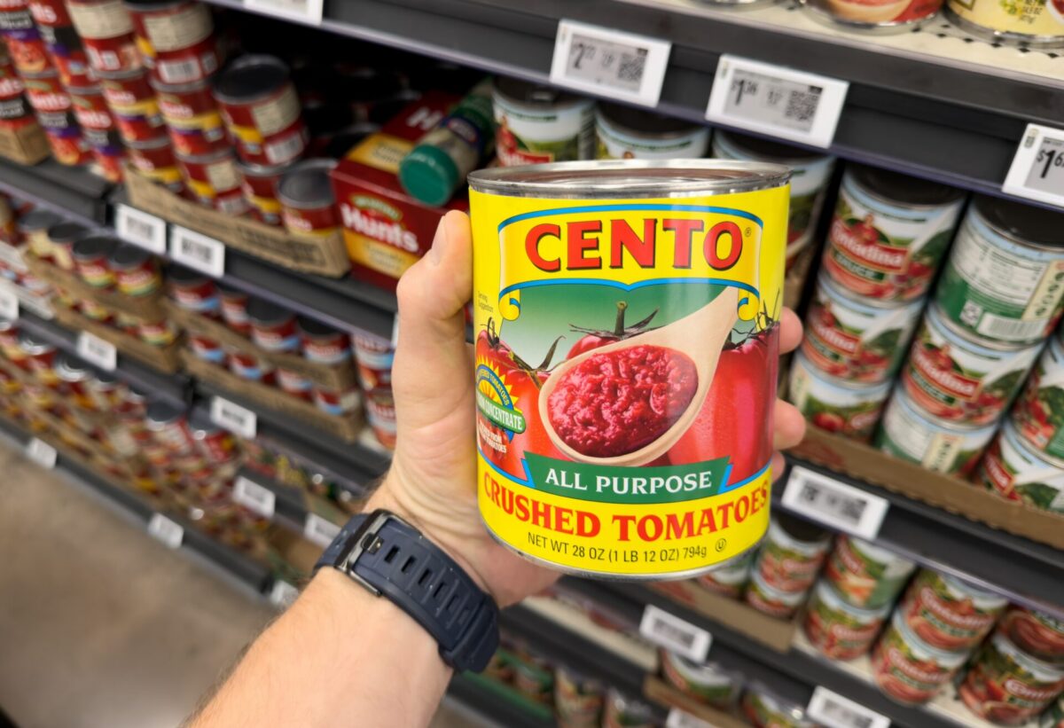 A hand holding a can of Cento crushed tomatoes in a grocery store aisle