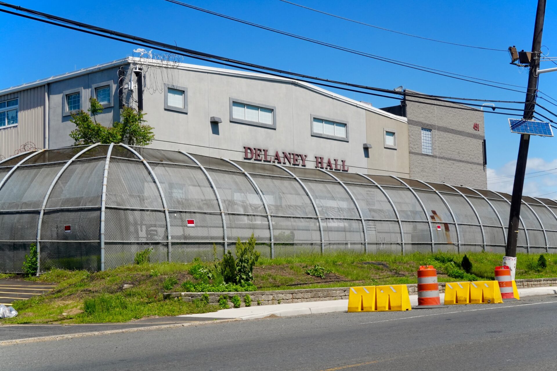 The exterior of Delaney Hall ICE detention facility in Newark, New Jersey, with security fencing and road barriers in the foreground
