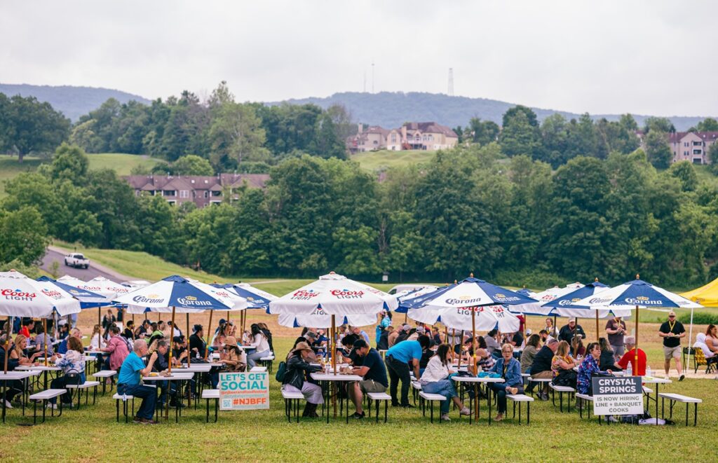 Crowds gather under Coors Light and Corona umbrellas at the NJ Beer & Food Festival on the Festival Field at Crystal Springs Resort in Hamburg, NJ, with the Sussex County hills in the background.