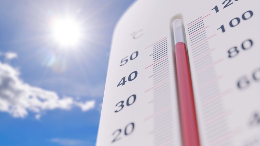 Close-up of a thermometer rising past 40 degrees against a blazing sun and blue sky, representing a severe summer heatwave that left at least 25 dead in New Jersey over July 4 weekend