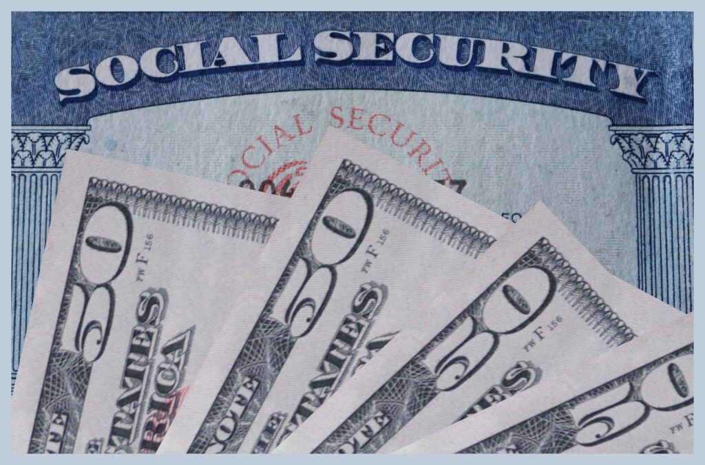 Social Security cards fanned out alongside U.S. currency, representing retirement benefit payments.