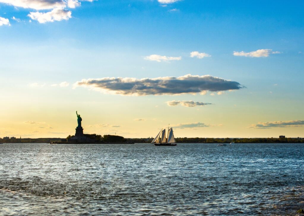 A sailboat passes the Statue of Liberty on New York Harbor, viewed from the New Jersey waterfront.