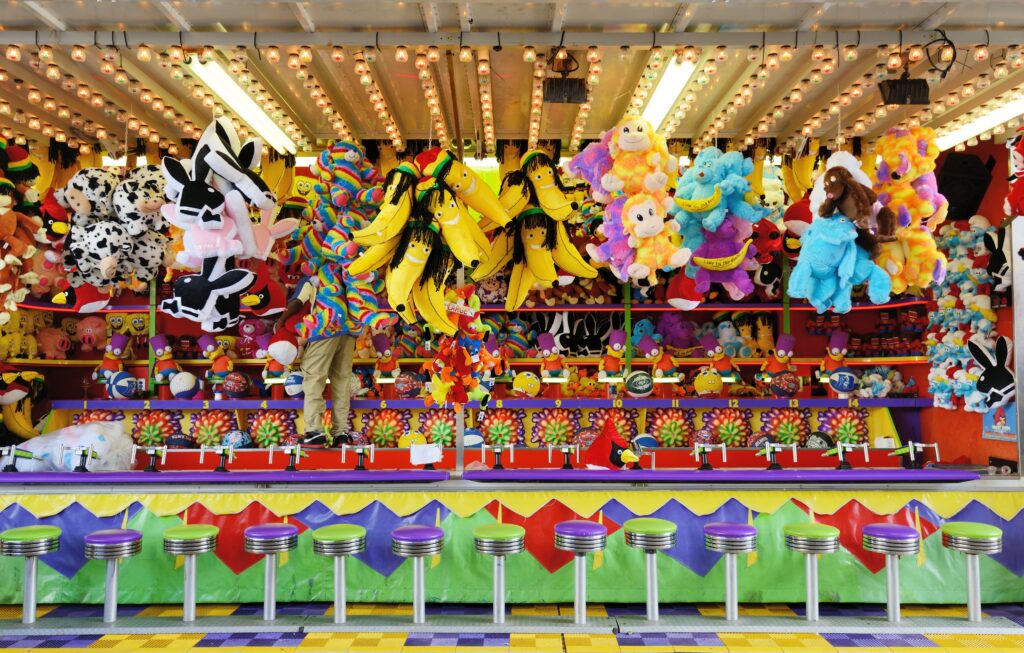 A colorful carnival midway game booth with plush prizes, similar to the games at the Middlesex County Fair