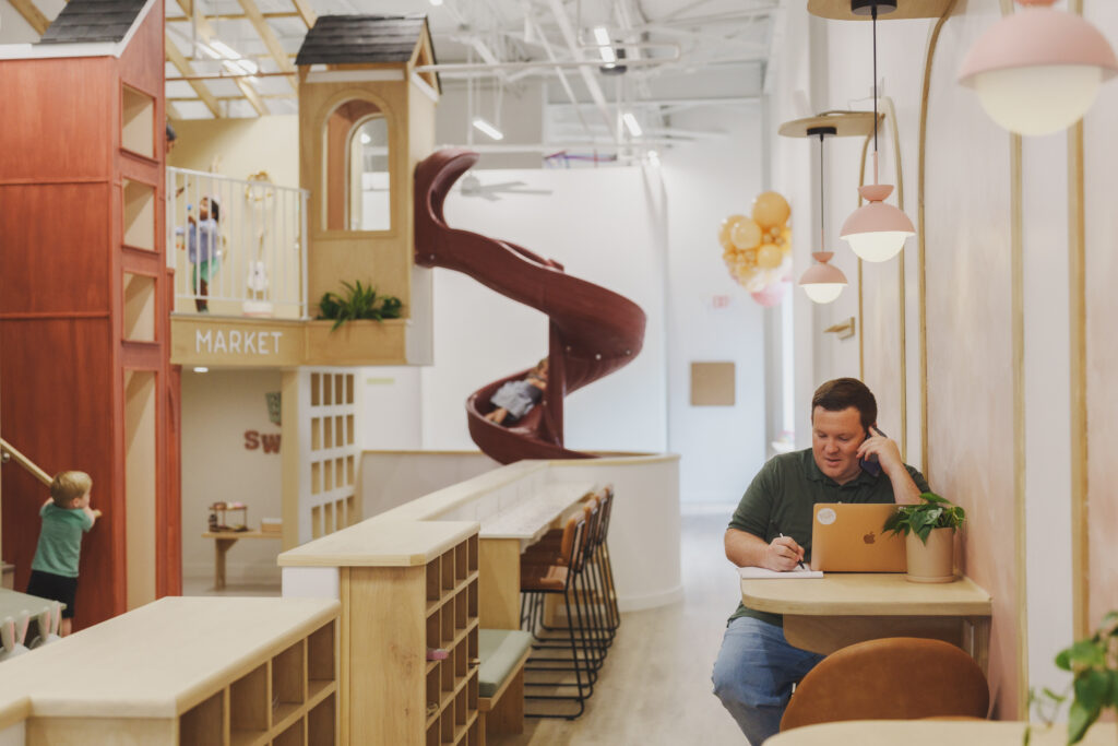an interior shot of a parent working at Small Town Play Café while his children play