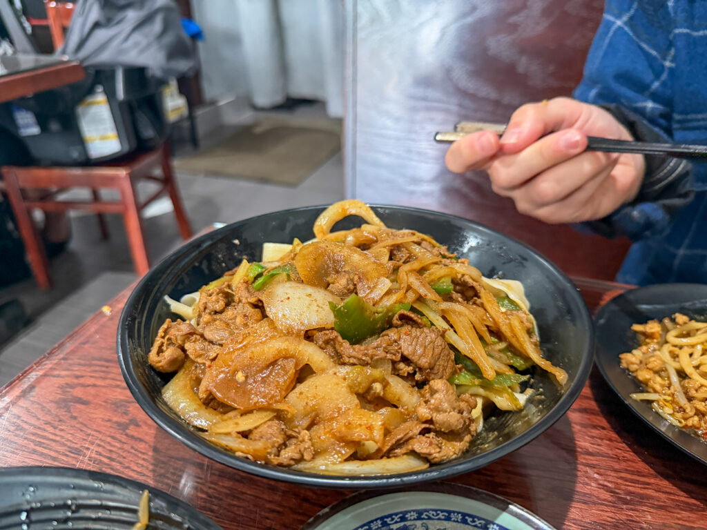a bowl of noodles with spiced lamb, peppers, and onions from Shan Shan Noodles