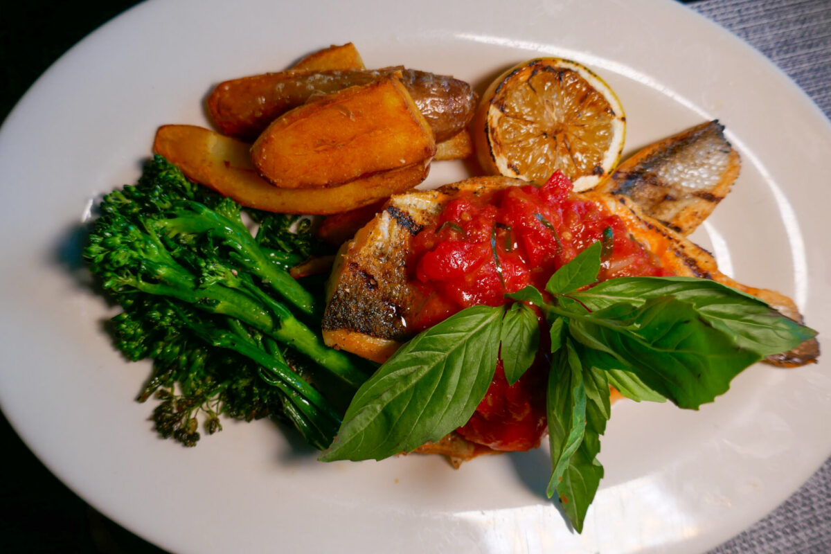Grilled Branzino on a white plate, topped with tomato chutney, basil, potatoes, and broccolini at Beneci's in Weehawken