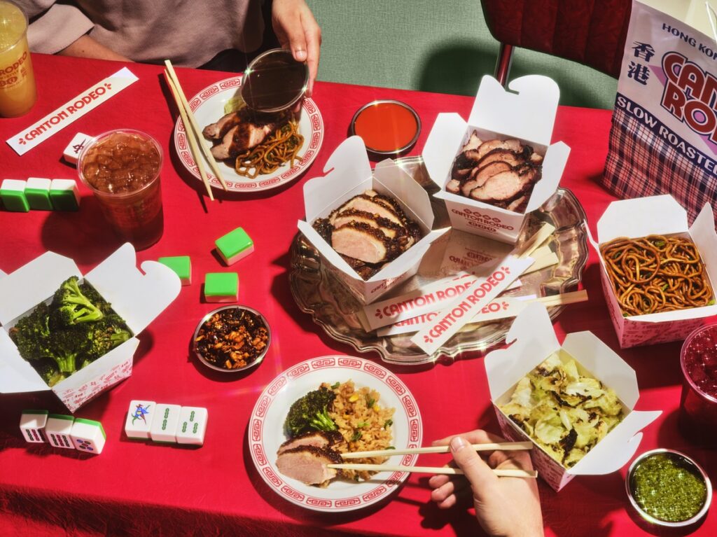 A spread of char siu pork, roast duck, noodles, and more on a red table at Canton rodeo