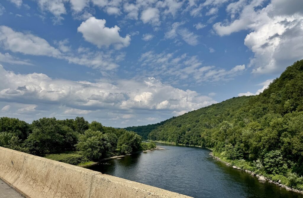 The Delaware River flowing through the New Jersey and Pennsylvania border, reflecting green tree-lined banks on a clear day